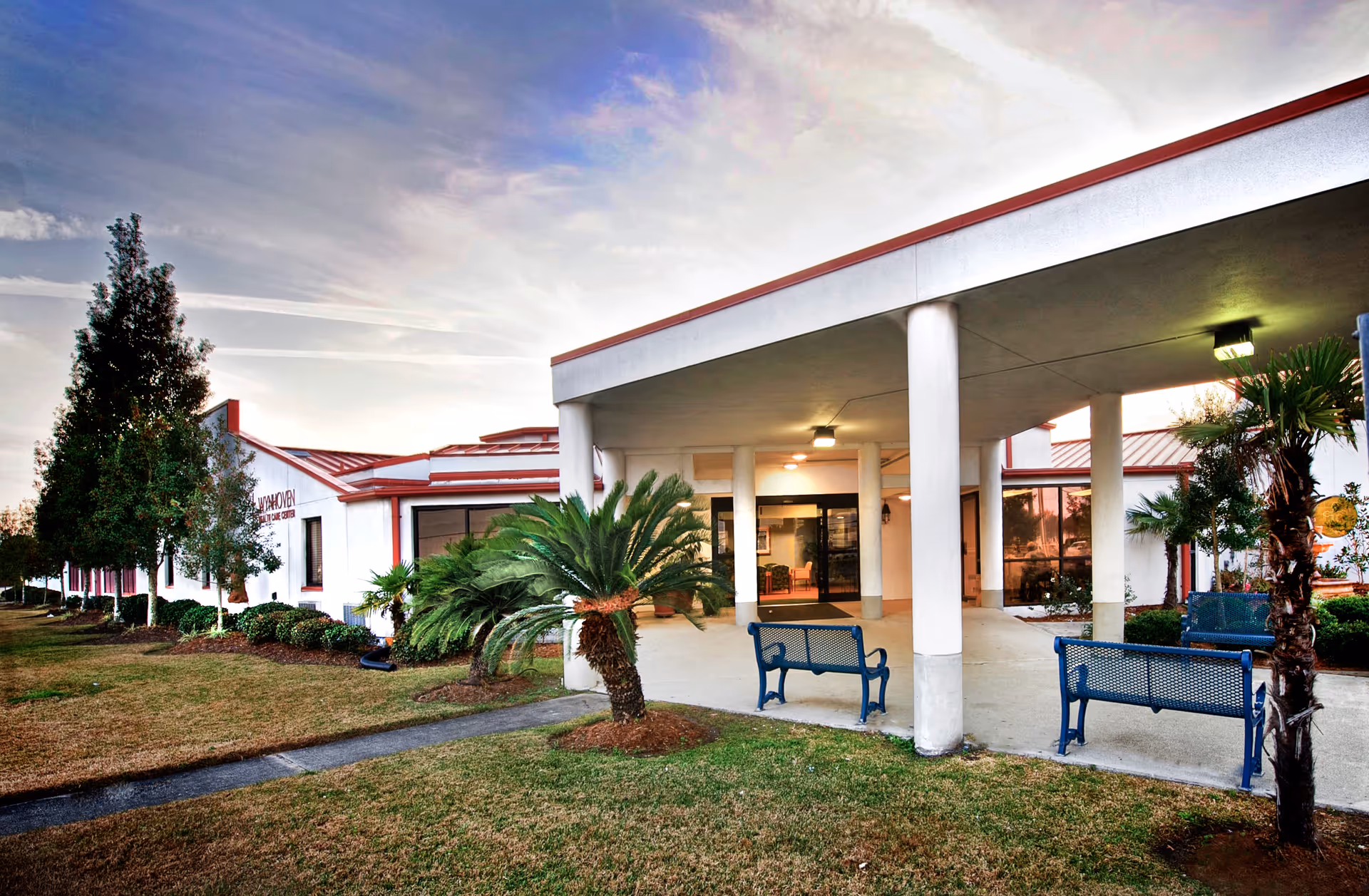 Exterior view of Wynhoven Health Care Center showing entrance, columns, palm trees, and benches.