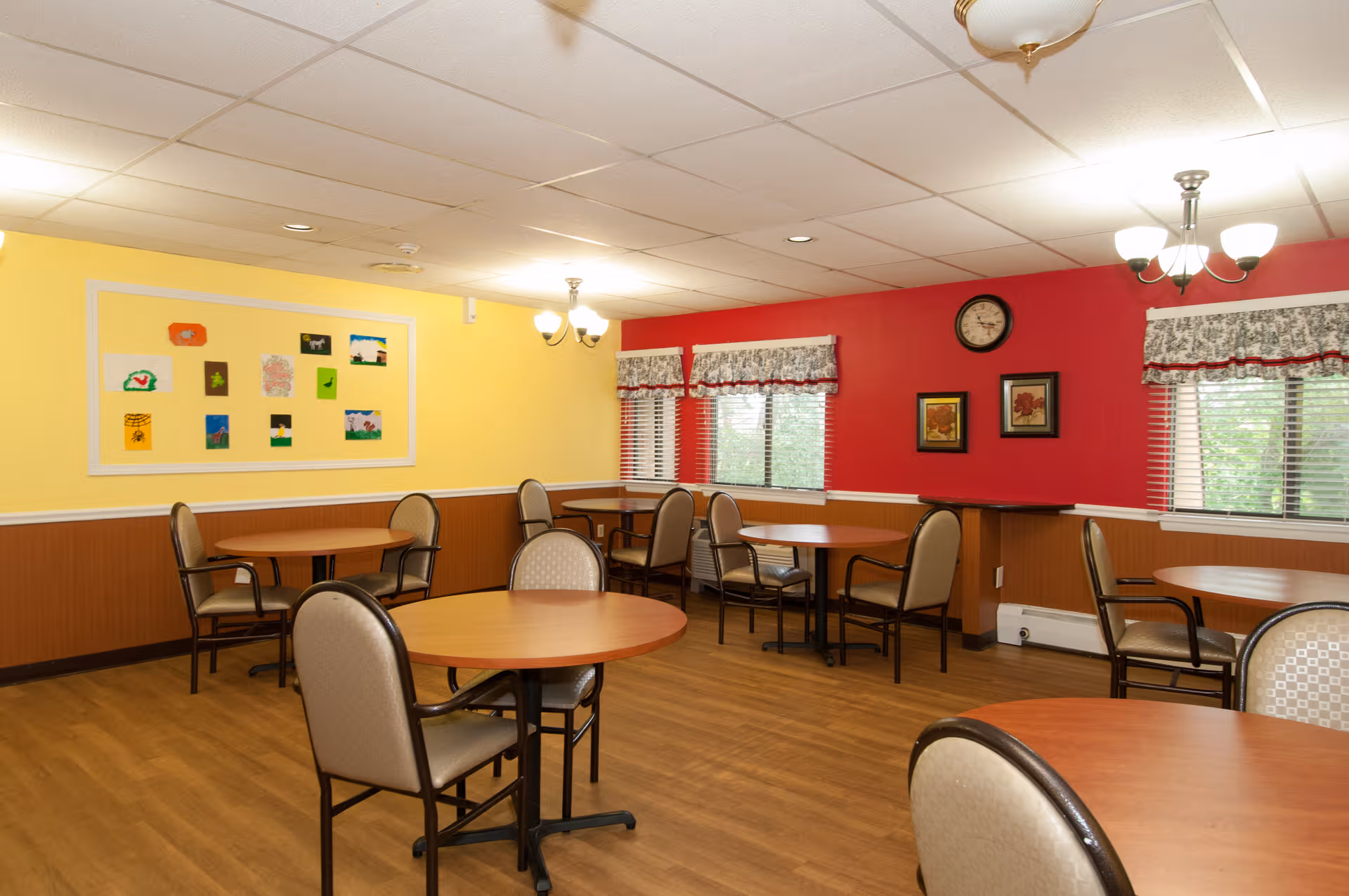 A bright communal dining room in Fresh River Healthcare, LLC with round tables.