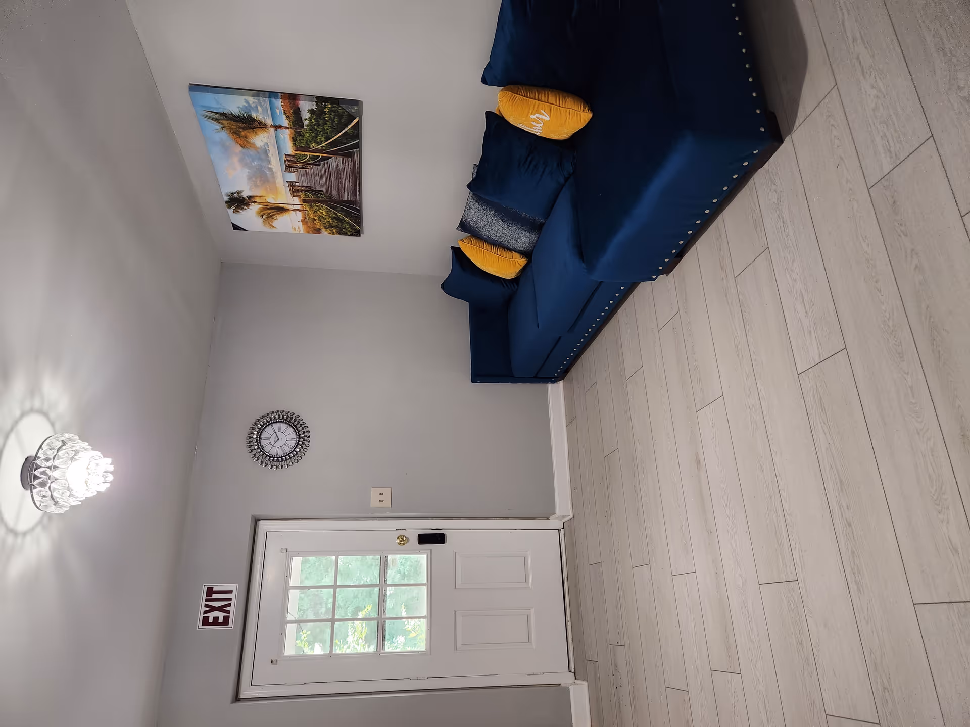 Small entry living area with a blue sofa, wall art, clock and a white door marked EXIT.