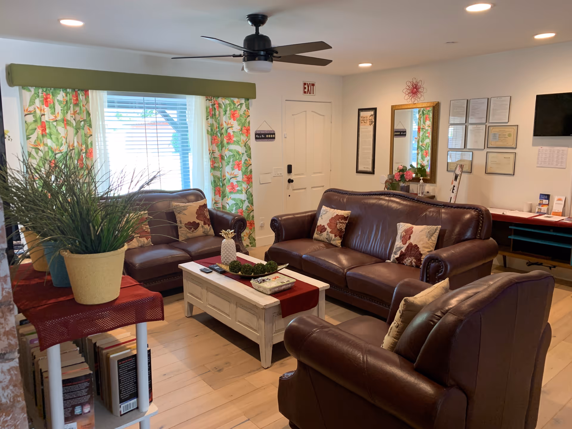 Cozy living room with leather sofas, coffee table, plants, and floral curtains in a senior lounge.