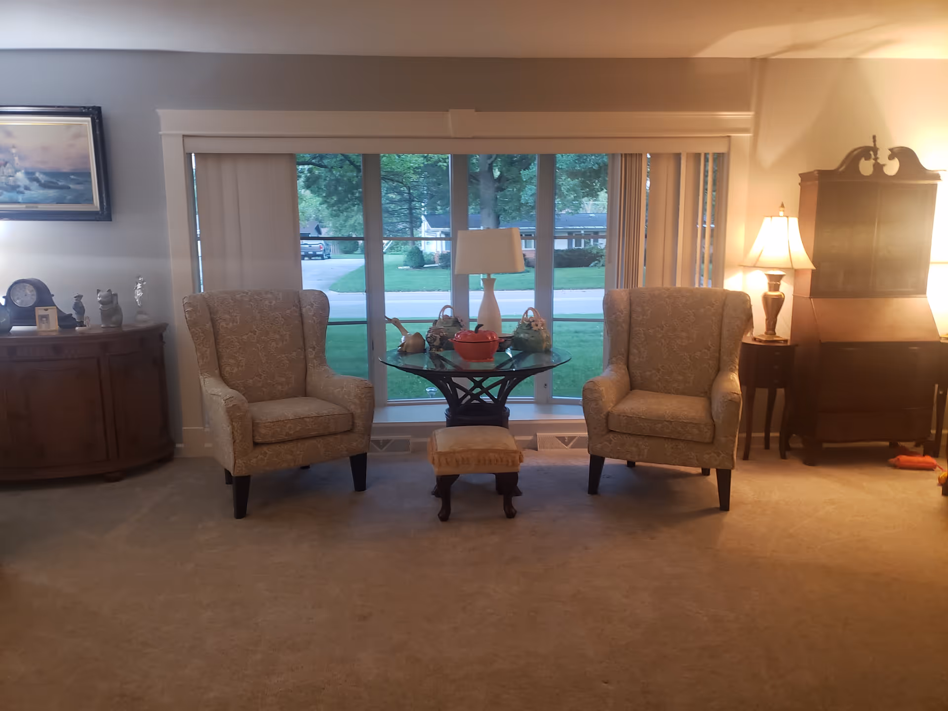 Cozy living room with two patterned armchairs, a glass table, and warm lamps.