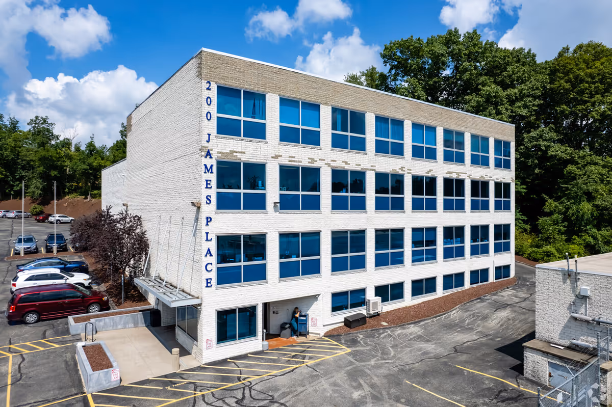Exterior view of a white brick, four-story building with blue windows and a parking area.