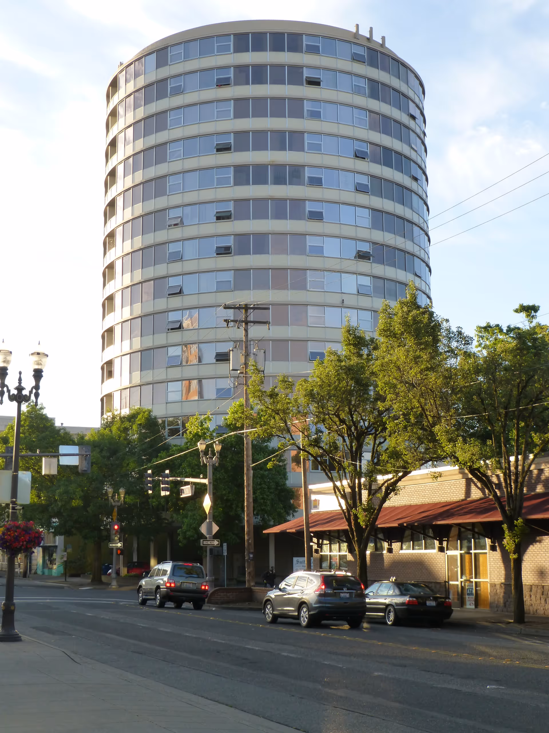 A tall, cylindrical multi-story apartment building named Smith Tower Apartments with many windows, situated on a street corner with trees, cars parked along the road, and street lamps.