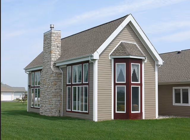 Exterior of Orchard Park Assisted Living building with beige siding, large windows, and a stone chimney.