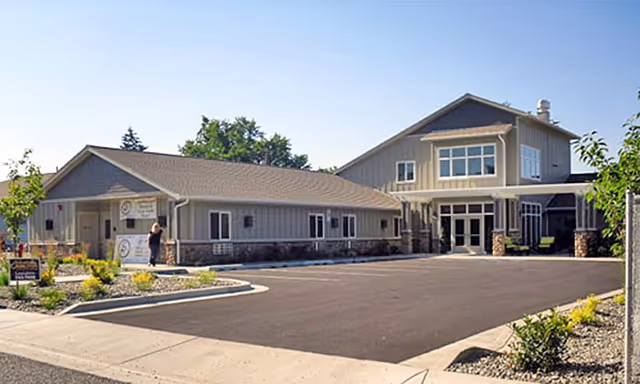 Front exterior of a beige single- and two-story senior living facility with a paved driveway and landscaped beds.