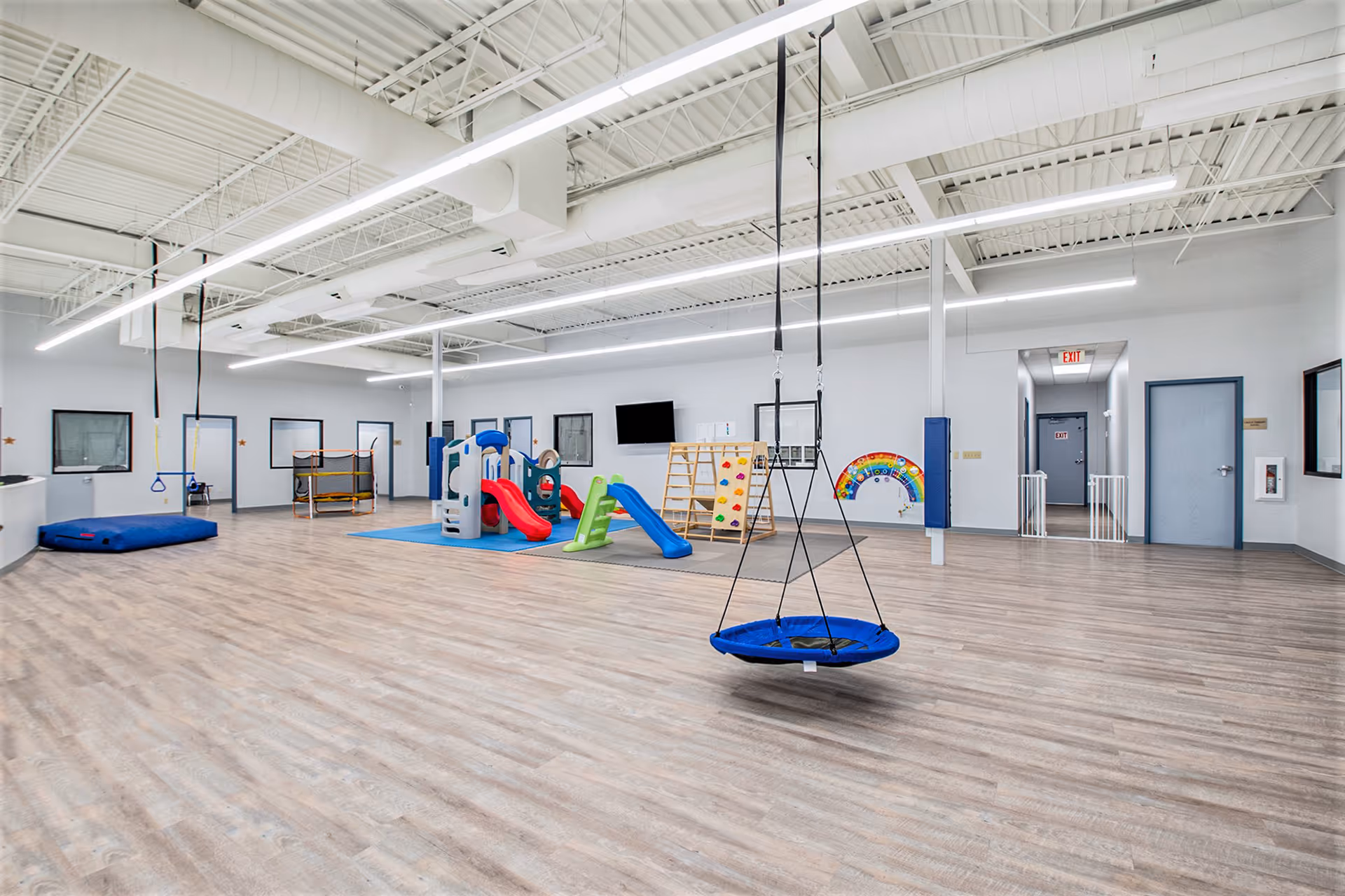Spacious indoor therapy room with a blue swing and colorful play equipment on wooden flooring