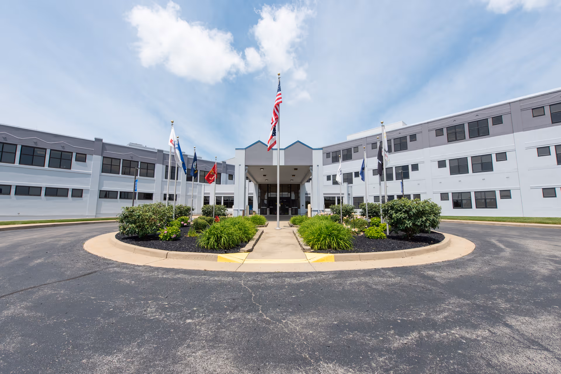 A modern hospital building with a circular driveway, flags, and landscaped entrance median.