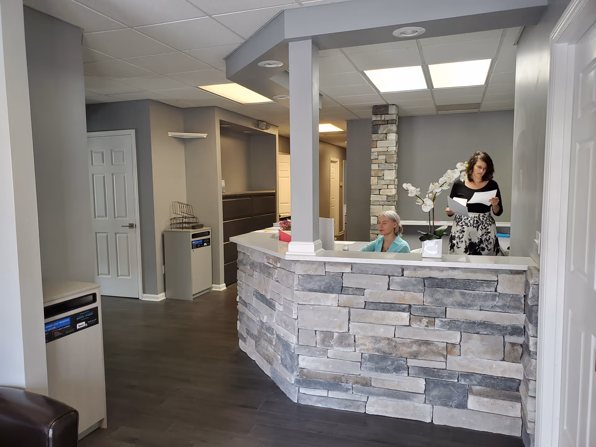 Stone-front reception desk inside a modern facility lobby with two staff members.