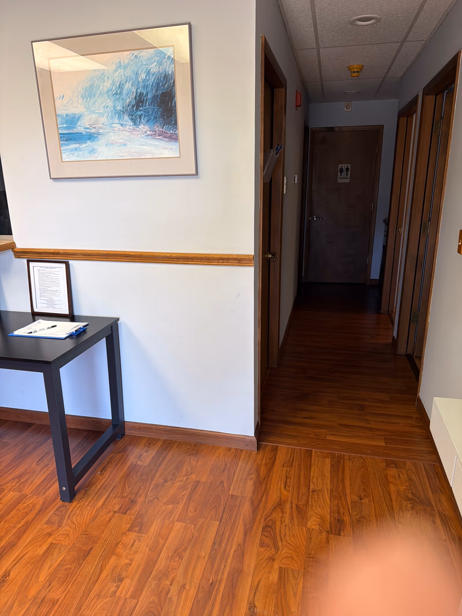 Interior hallway in a senior living facility with a side table, wall art, and closed doors.