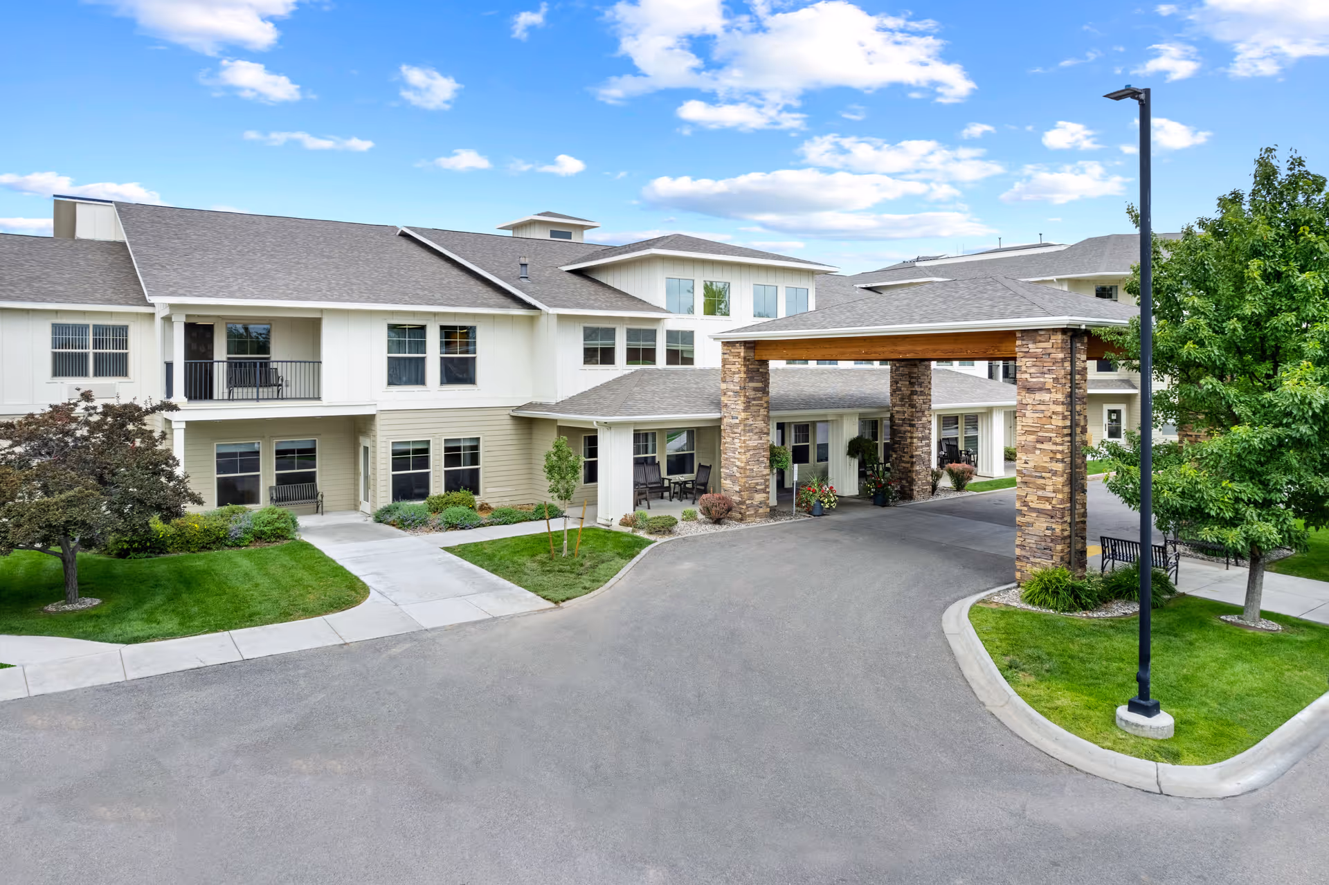 Front entrance and porte-cochère of a two-story senior living facility with landscaped lawns and a curved driveway.