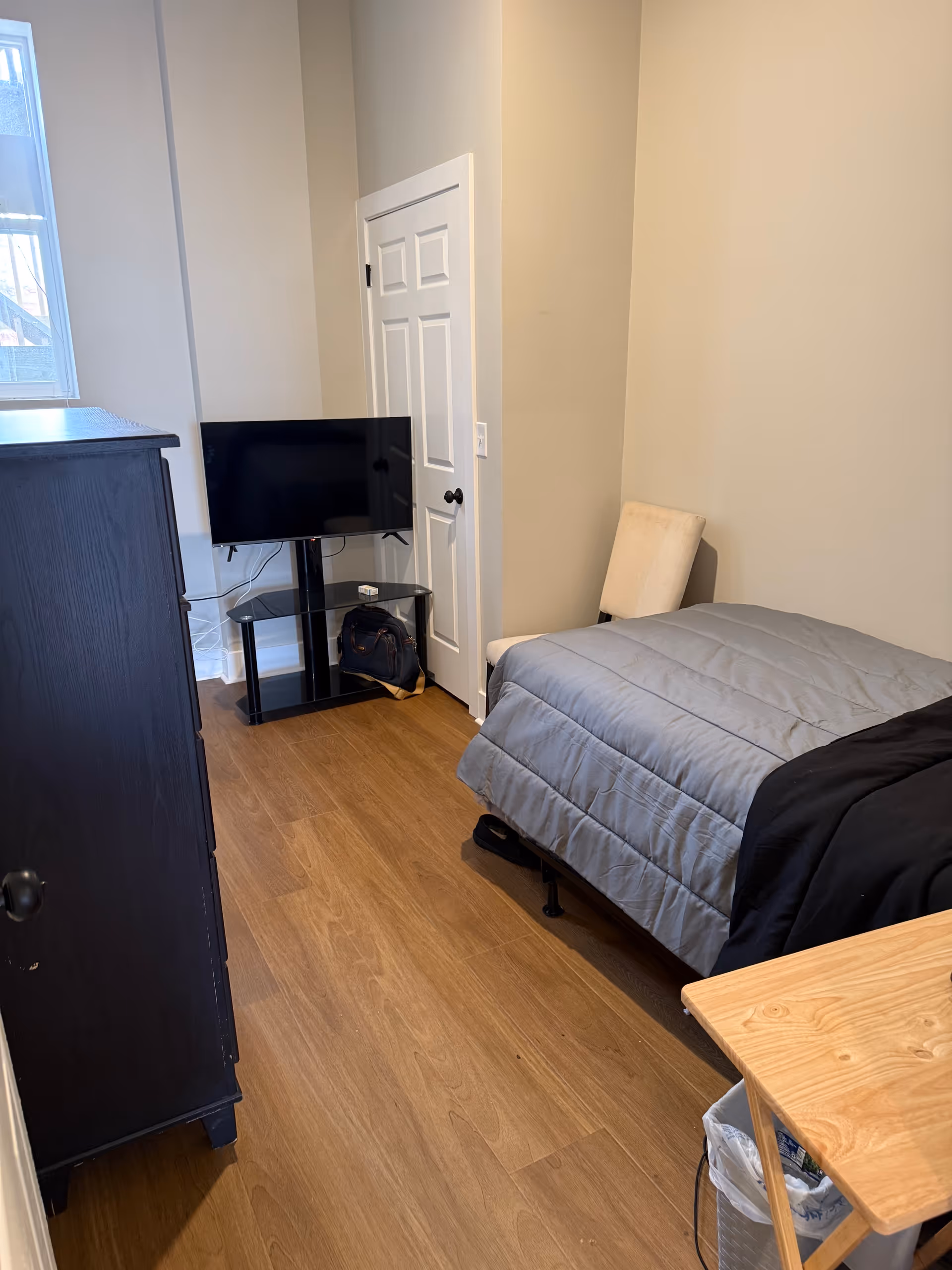 Small bedroom in Nirvana House Assisted Living with bed, dresser, TV, and chair.