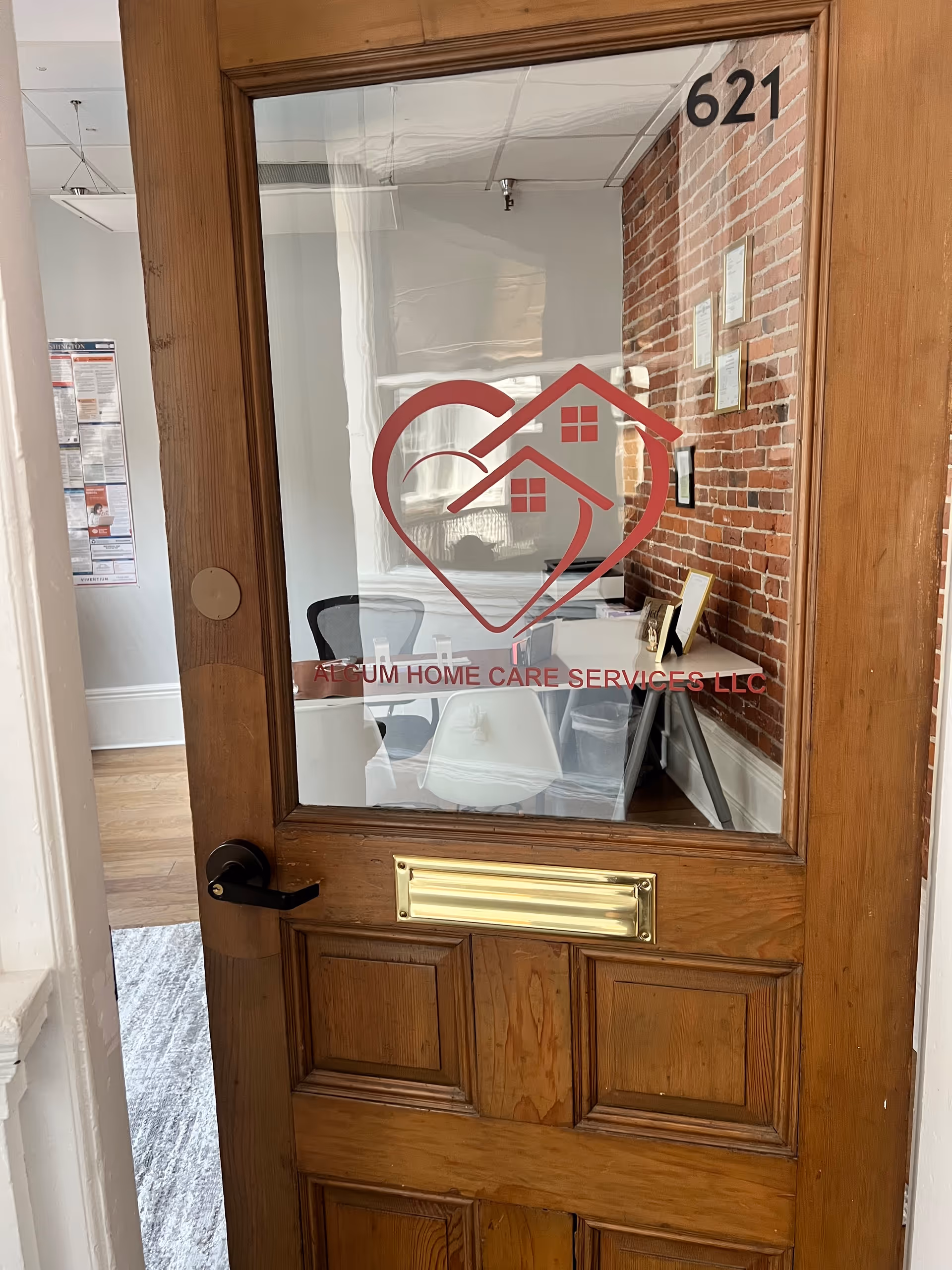 Wooden door with glass panel displaying Algum Home Care Services logo; brick-walled interior visible.