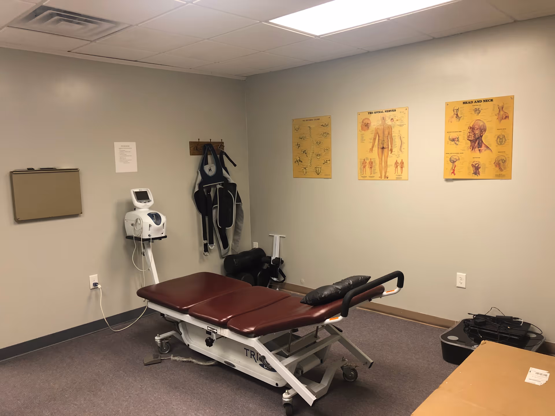 Medical examination room with burgundy therapy table, equipment, and wall charts.