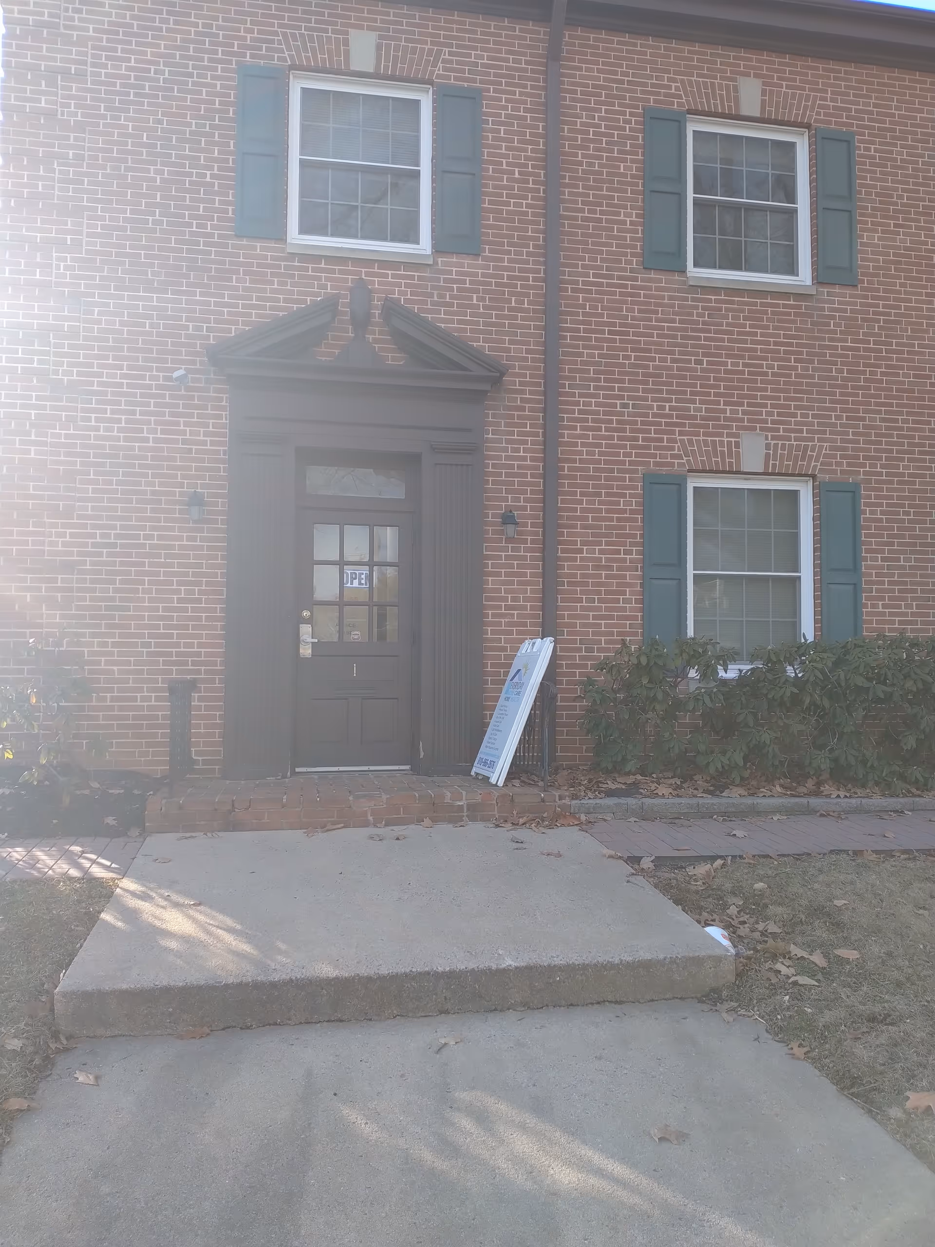 Brick building entrance with a black door, green shutters, and a signboard outside.