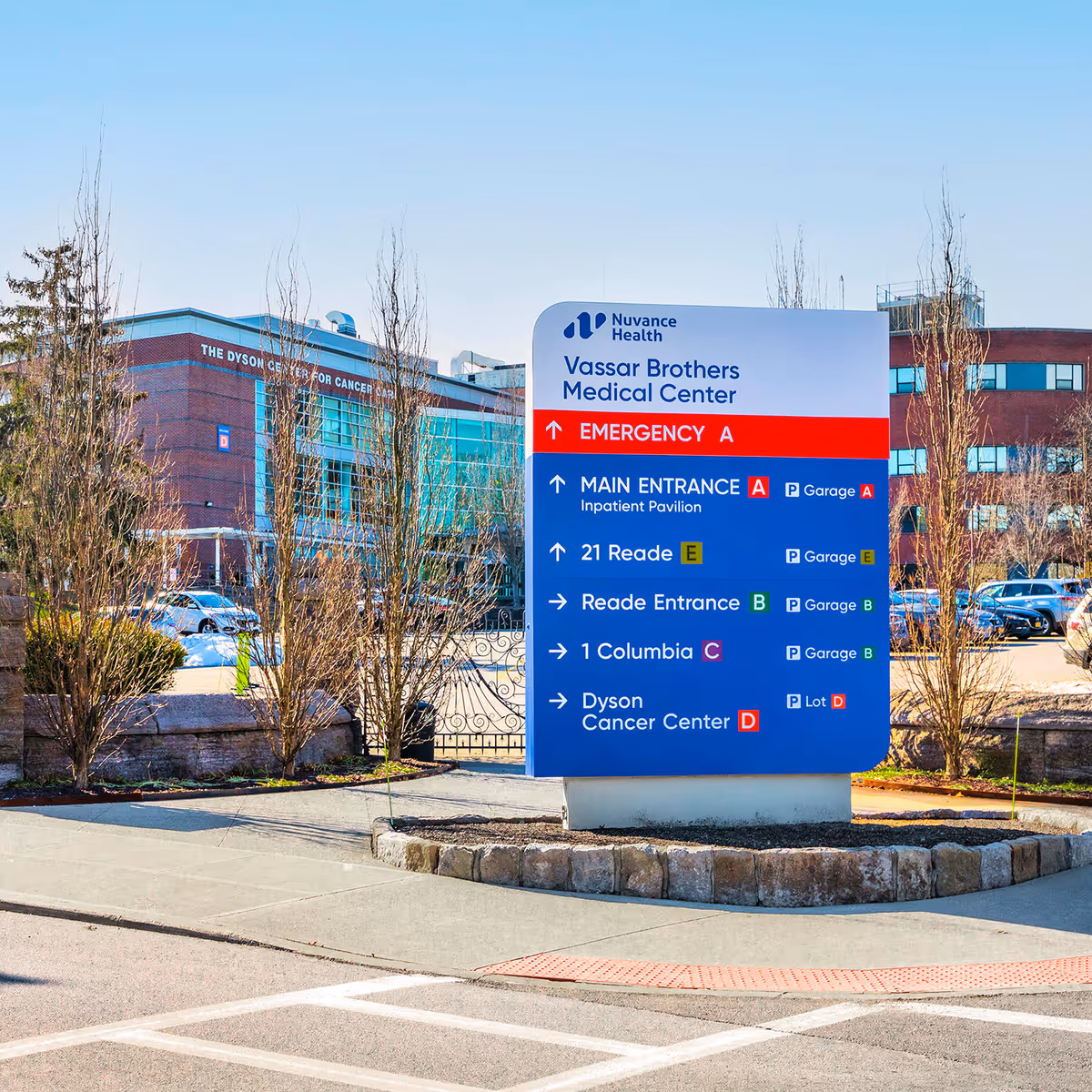 Large blue hospital directional sign outside Vassar Brothers Medical Center with building in background.