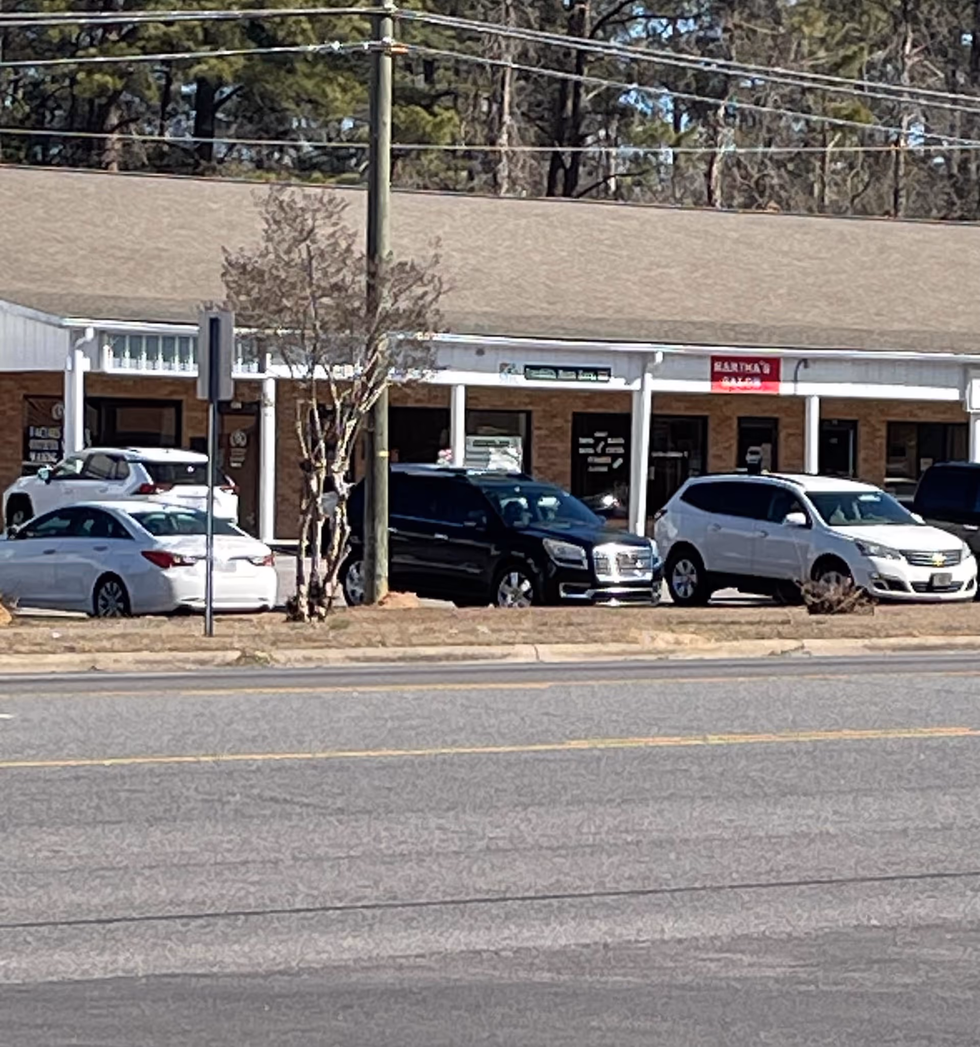 Exterior of a strip mall with storefronts and parked cars.
