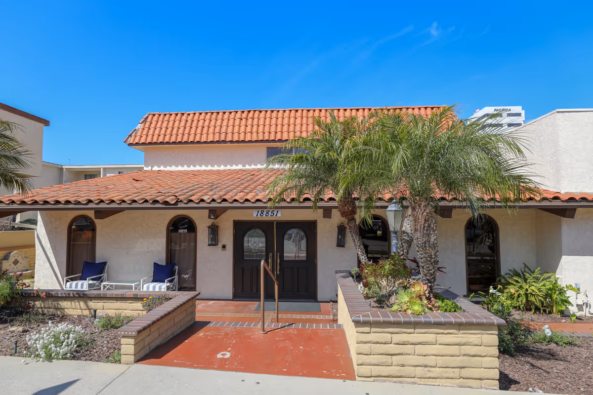 The front exterior of Sea Cliff Assisted Living with red roof, double doors, and palm trees.
