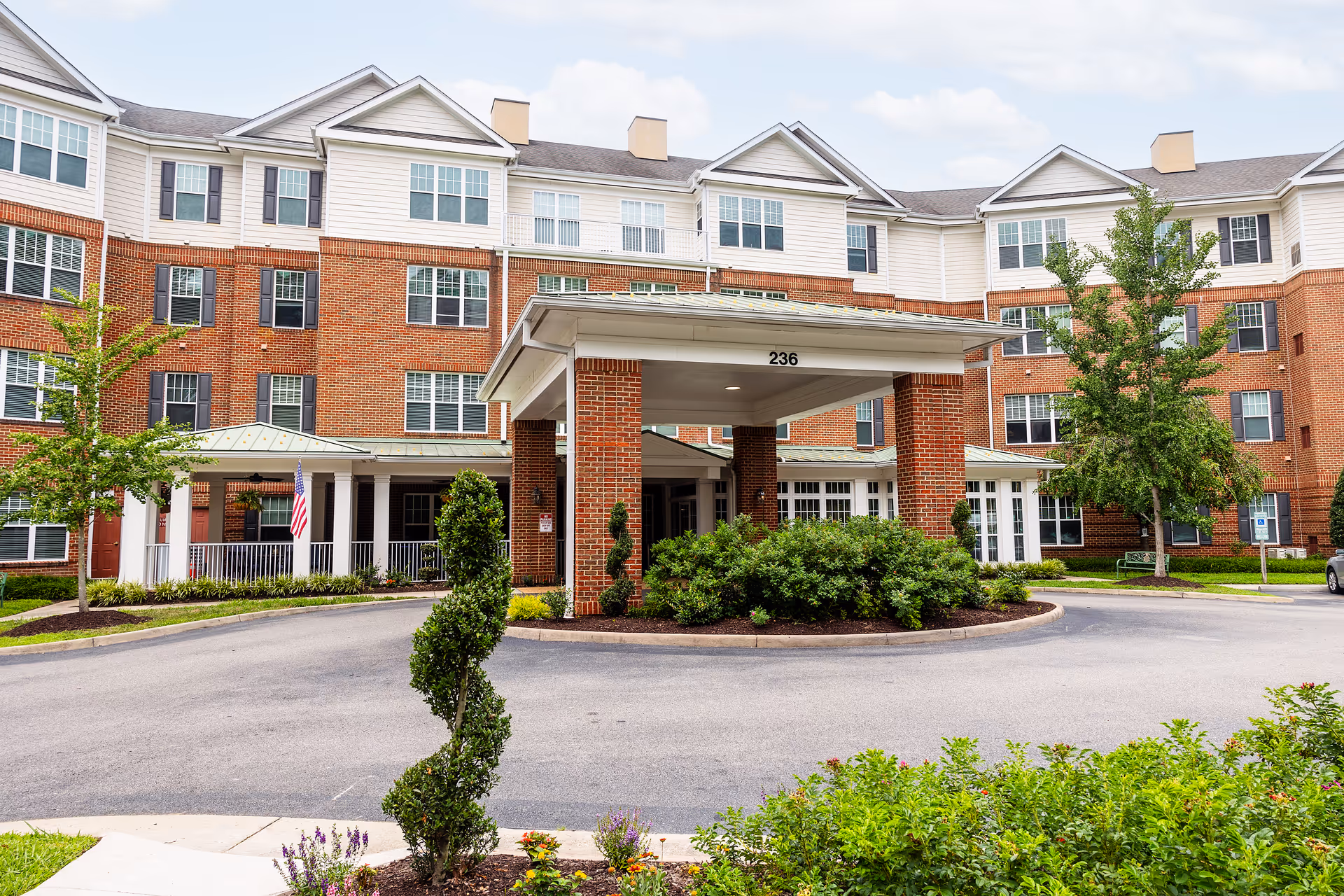 Brick senior living building with canopy entrance, circular driveway, and landscaped surroundings.