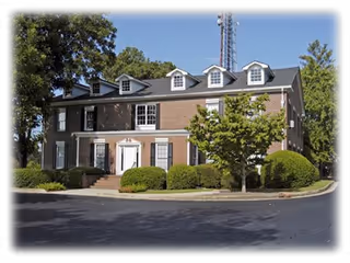 Brick senior living facility front exterior with steps, shrubs, and a tree.