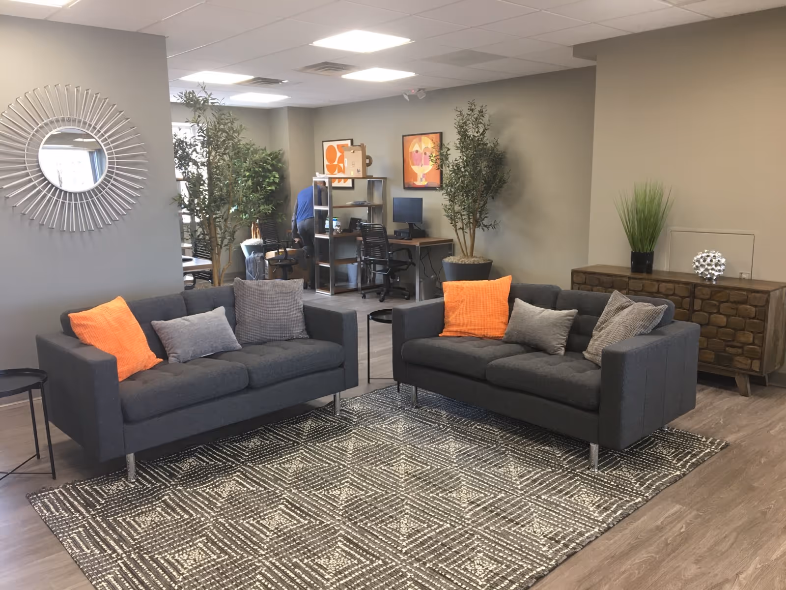 Two dark gray sofas with orange pillows surround a patterned rug in a modern lounge.