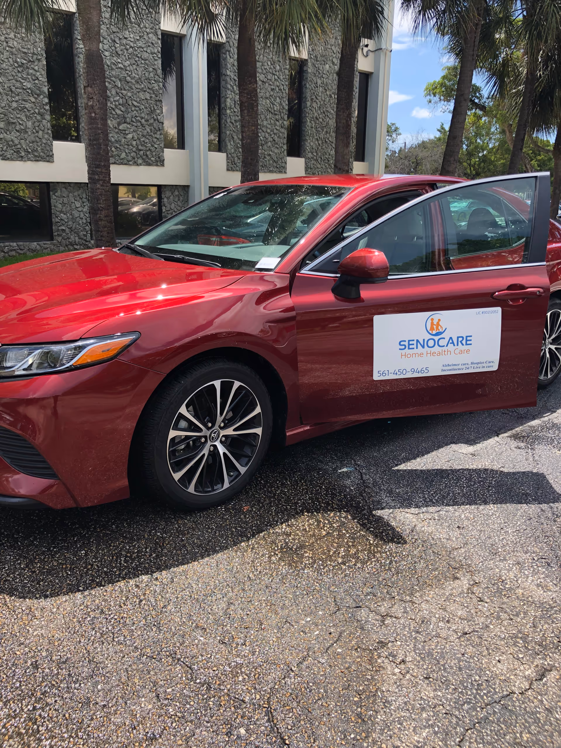 Red Senocare-branded car parked outside a building with palm trees.