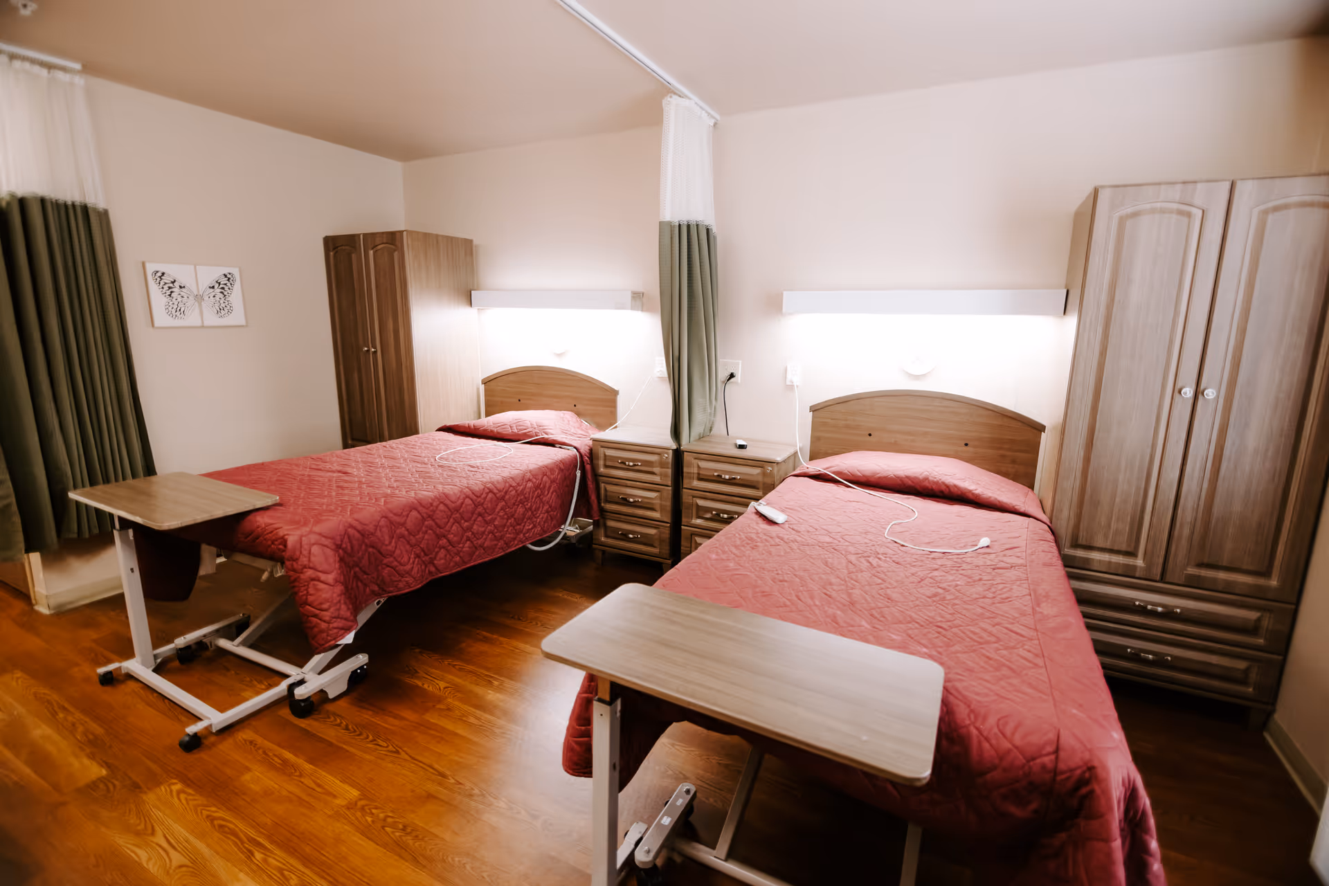 Two twin beds with red quilts and wooden furniture in a shared senior bedroom.