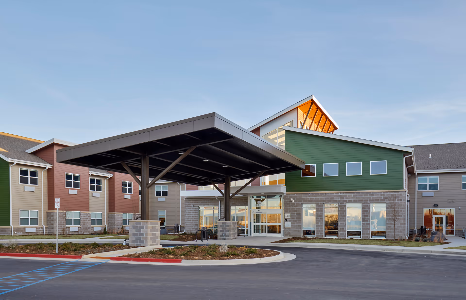 Front entrance of a modern senior living building with a large covered drop-off canopy and multi-colored siding.