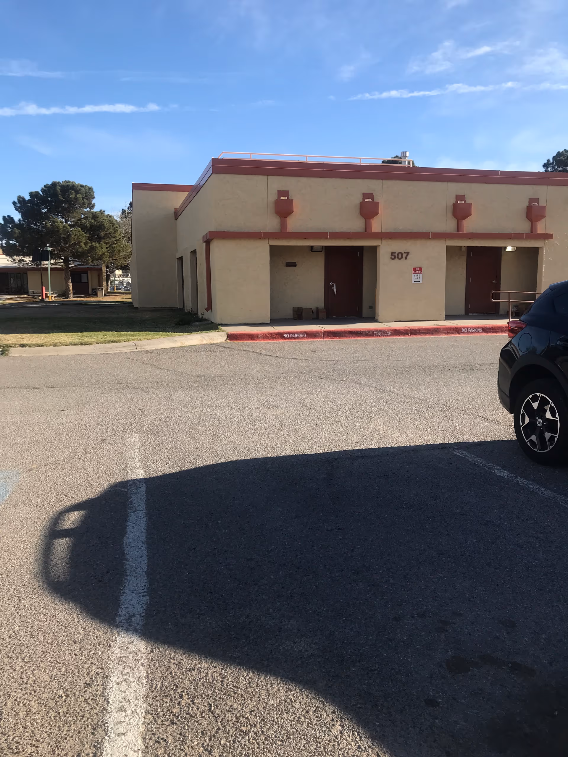 Exterior view of a beige building with red trim and a parked car.