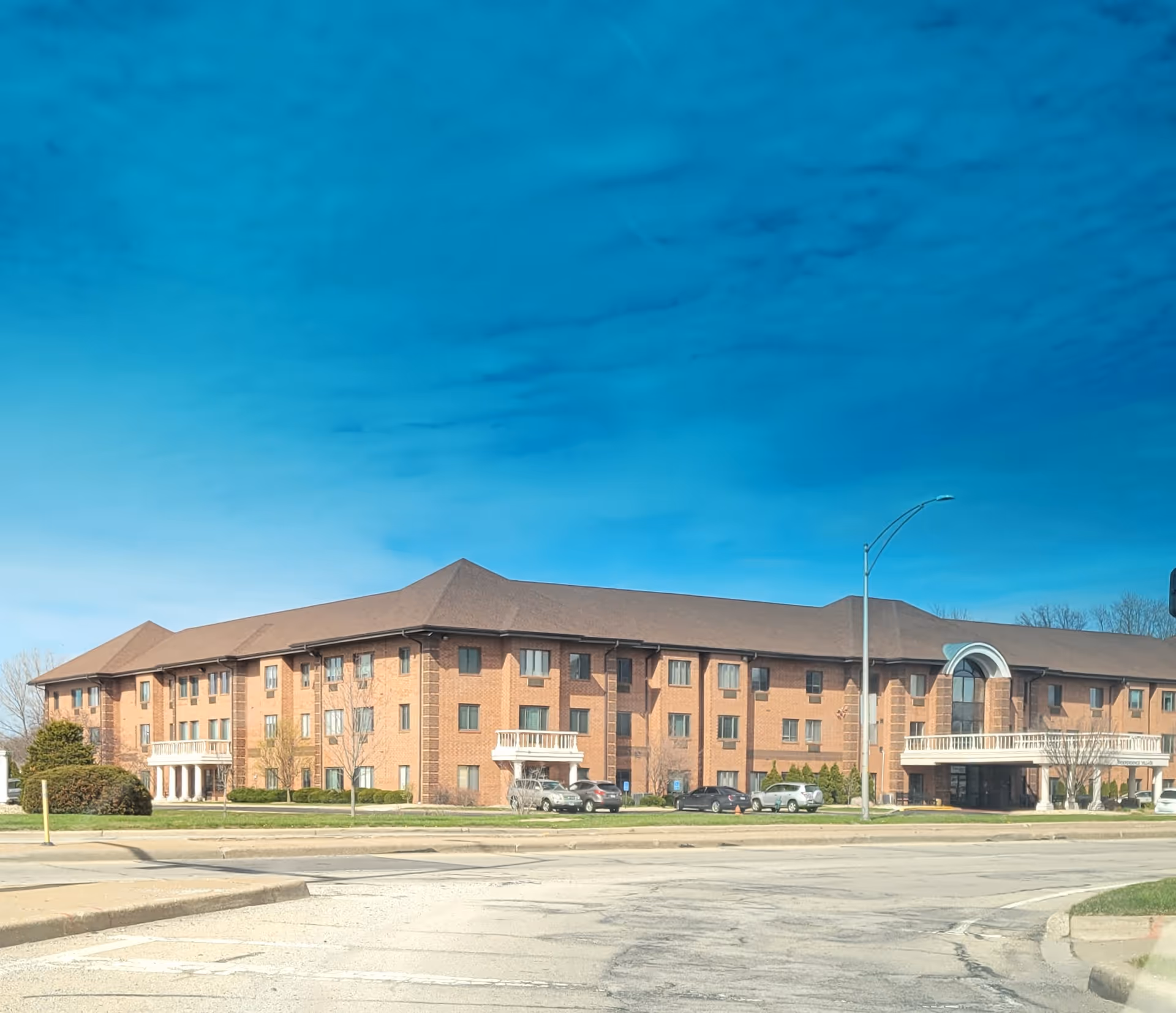 Brick senior living facility exterior with parked cars and a curved entrance.