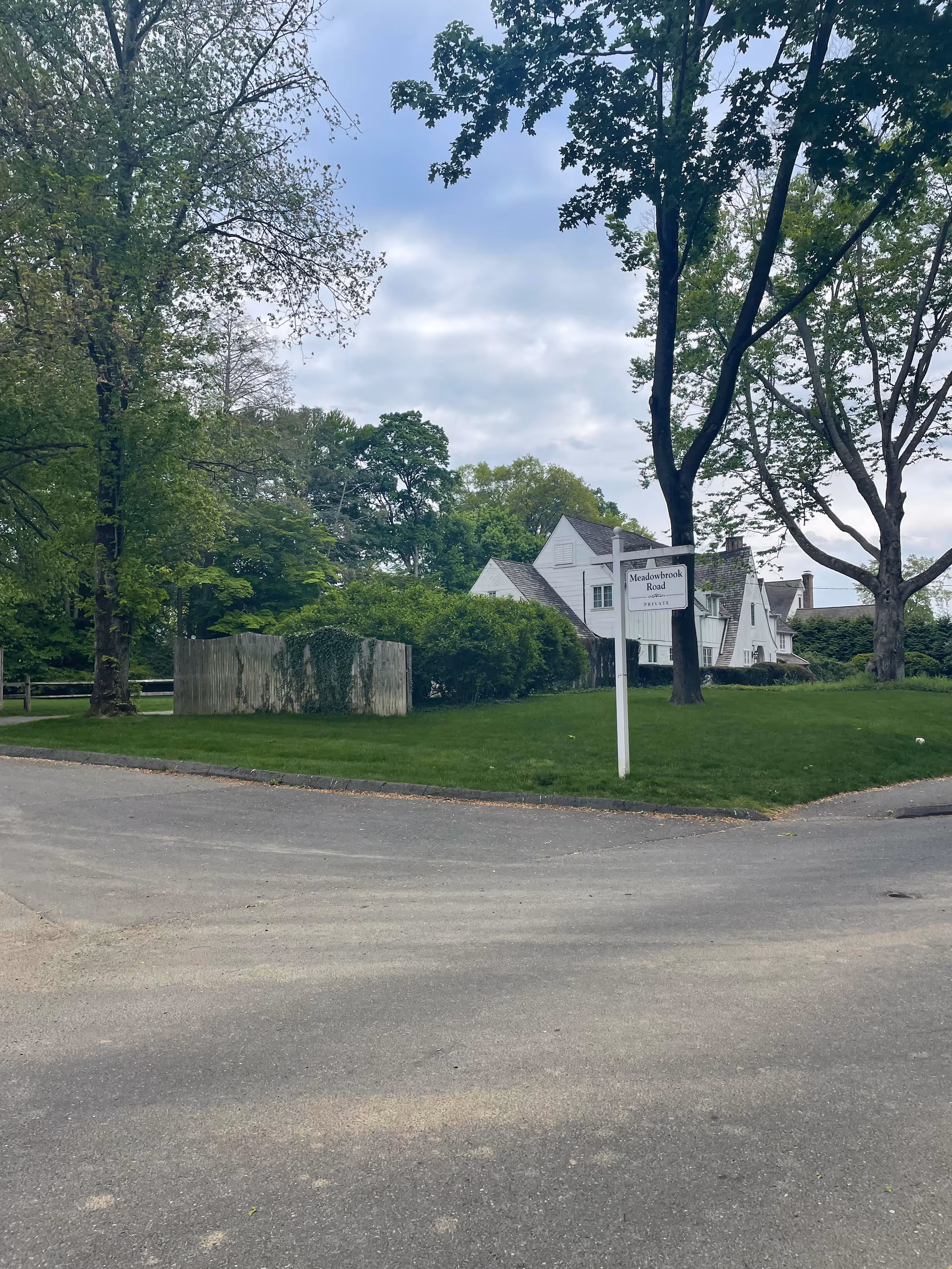 A quiet suburban street view with a white building and Meadowbrook Road sign among trees.