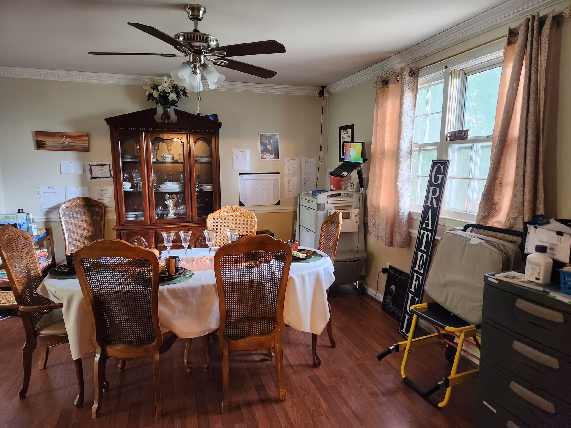 Dining room with a round table set for a meal, china cabinet, and windows.