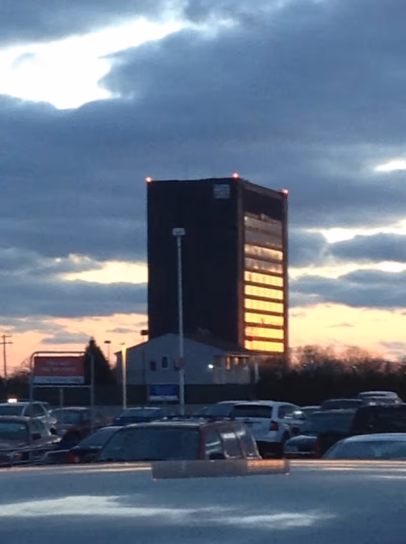 Tall dark building with sunset-reflected windows in a crowded parking lot.
