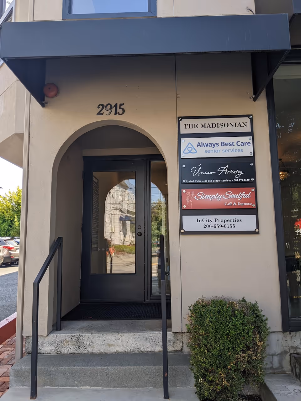 Beige building exterior with arched doorway, steps, and multiple tenant signs.
