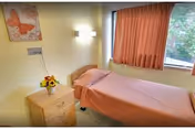 A small bedroom with a single bed, nightstand, lamp, and pink curtains.