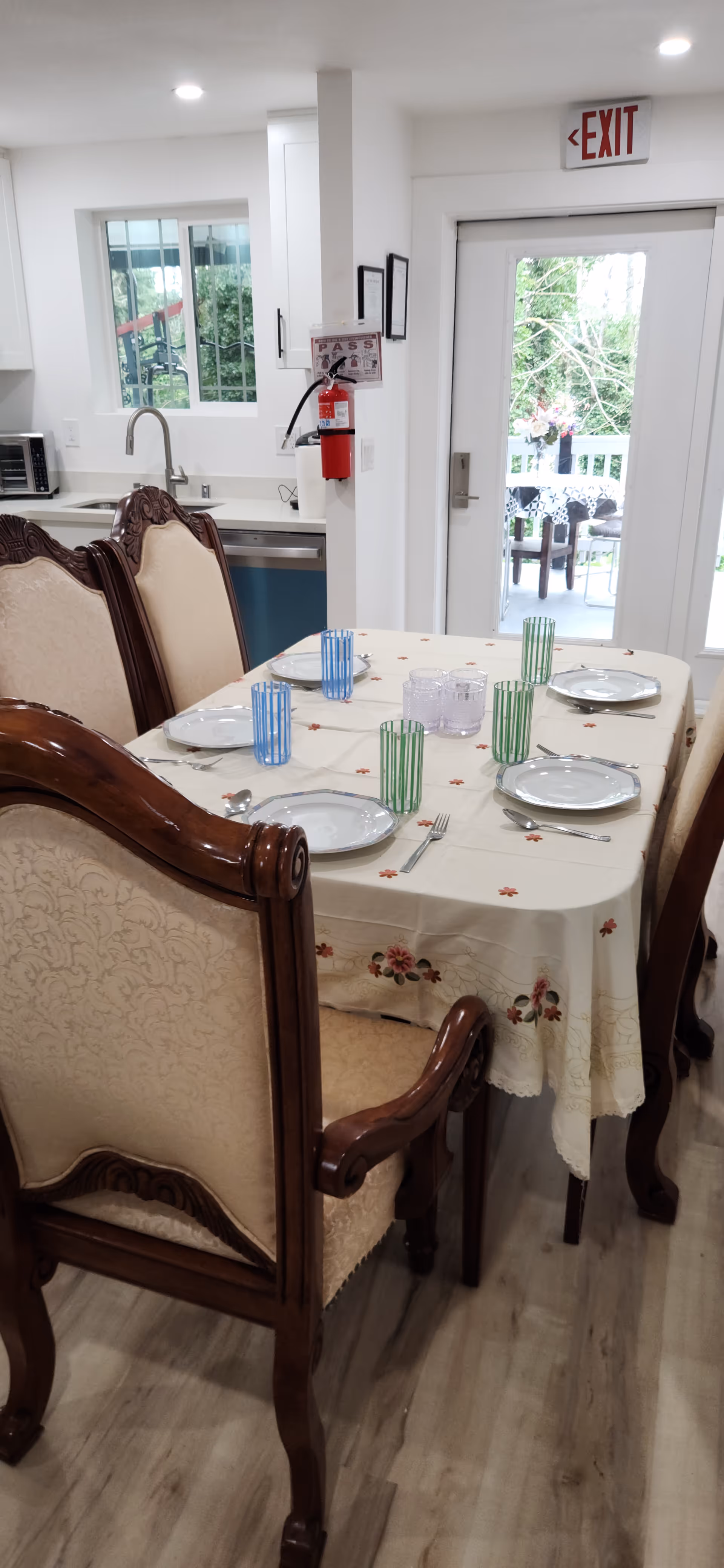 Dining room with a table set for a meal, ornate chairs, and a bright kitchen nearby.