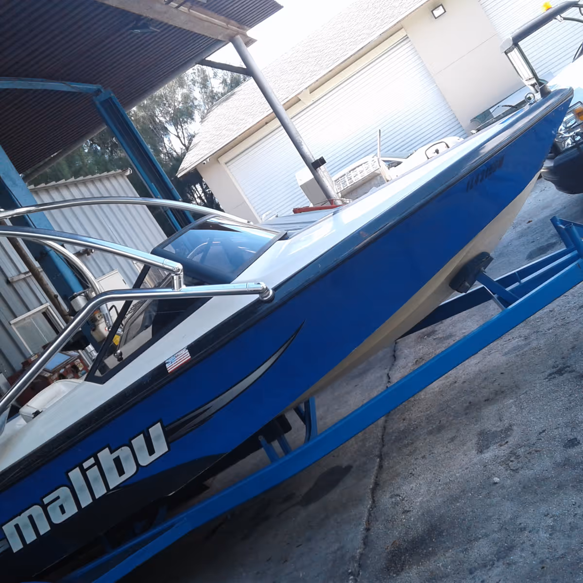Blue Malibu speedboat on a trailer beside a white building outdoors