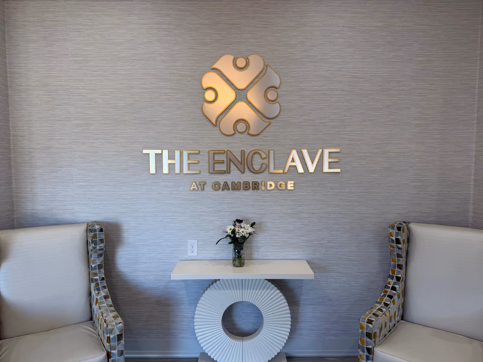 Lobby seating area with a small table, flowers, and wall signage reading The Enclave at Cambridge.