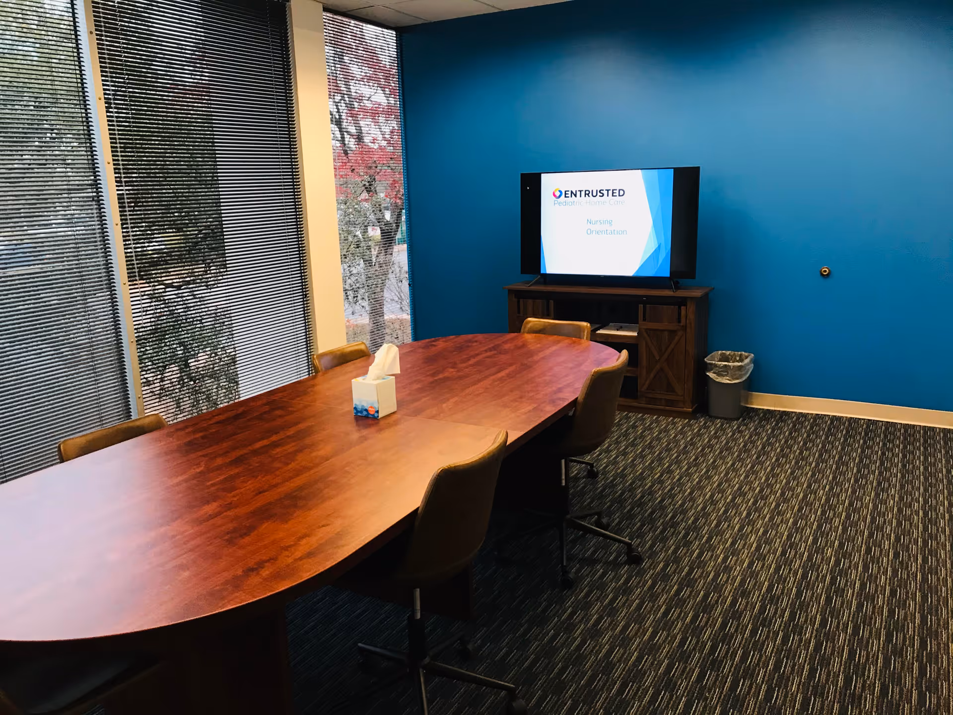 Conference room with a long table, chairs, blue wall, and TV displaying Entrusted Pediatric Home Care.