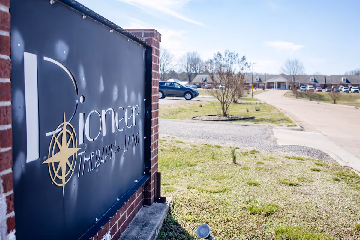Brick entrance sign reading 'Pioneer' beside a driveway leading to a low-rise nursing home building and parking lot.