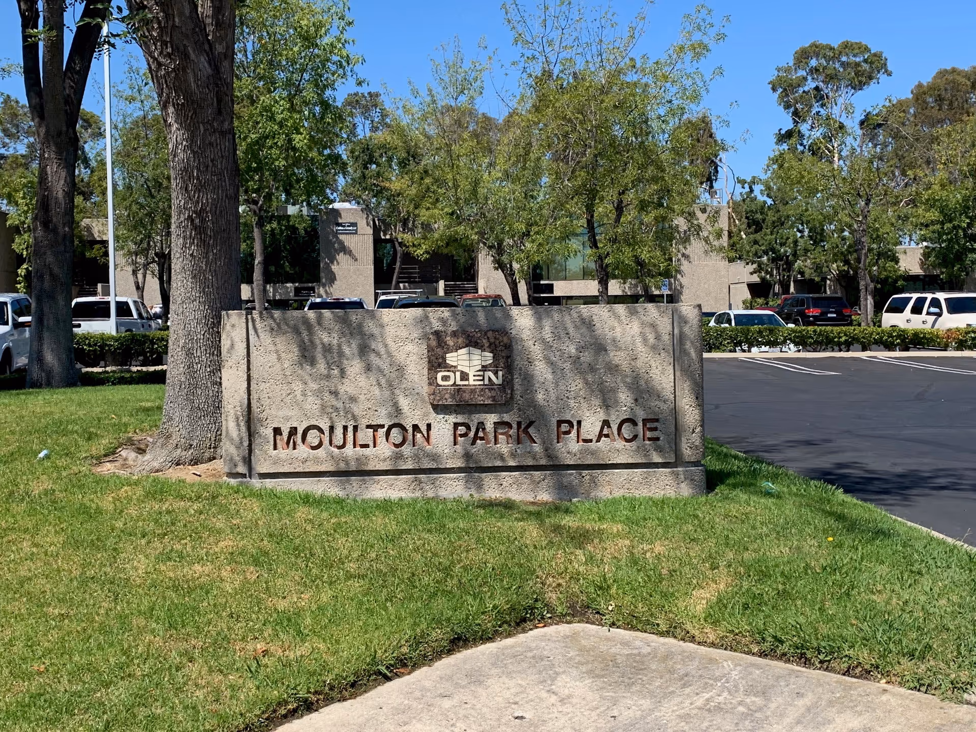 Exterior view of a stone sign reading Moulton Park Place in a grassy, tree-lined lot.