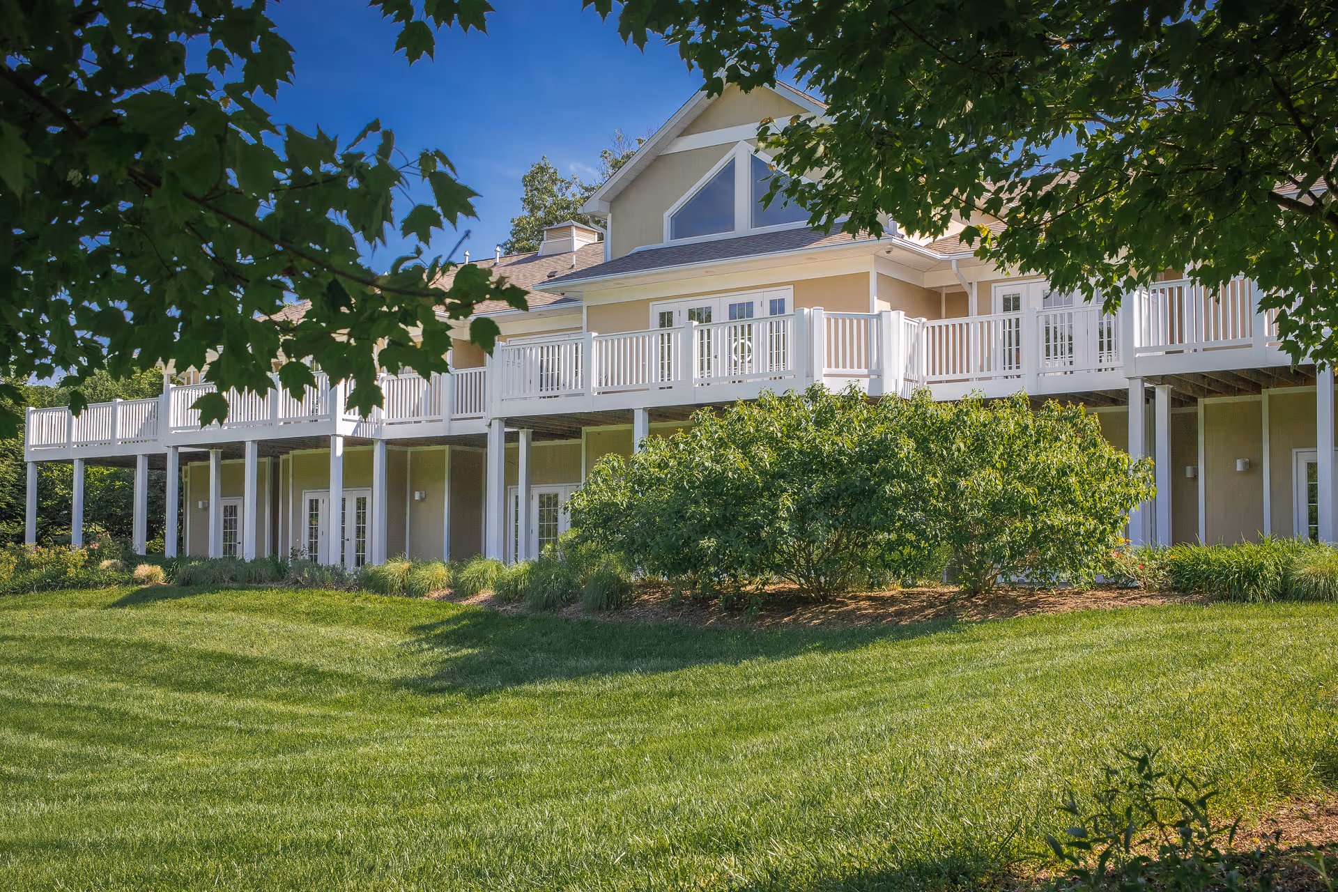 Two-story hospice house with white balconies, beige siding, and a neatly mowed lawn.