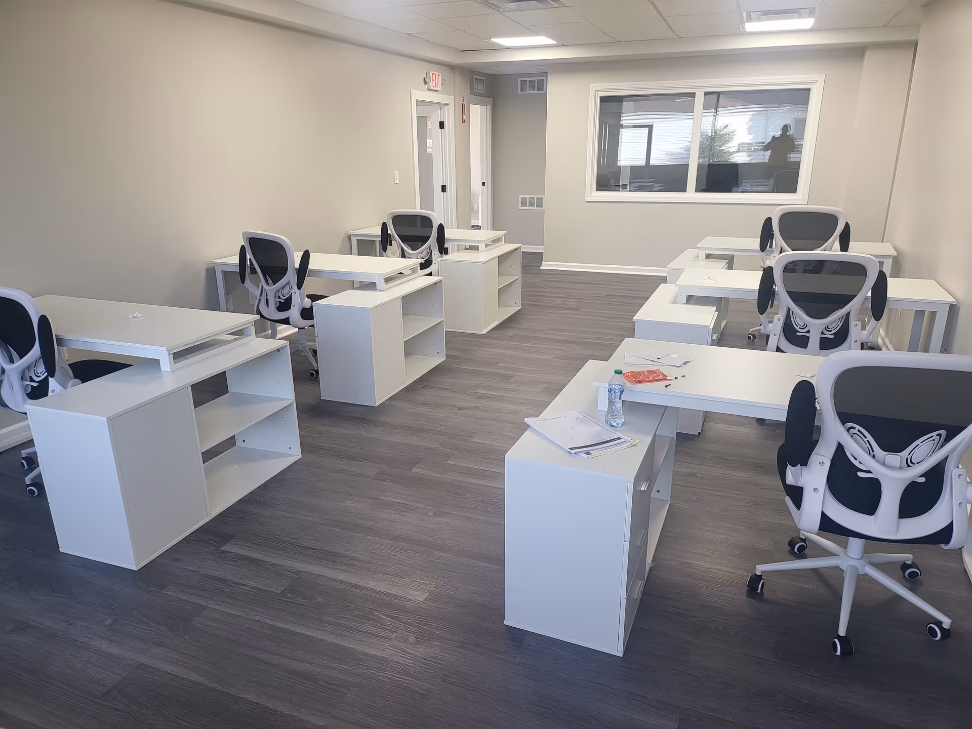 Empty interior room with white desks and ergonomic chairs arranged in rows.