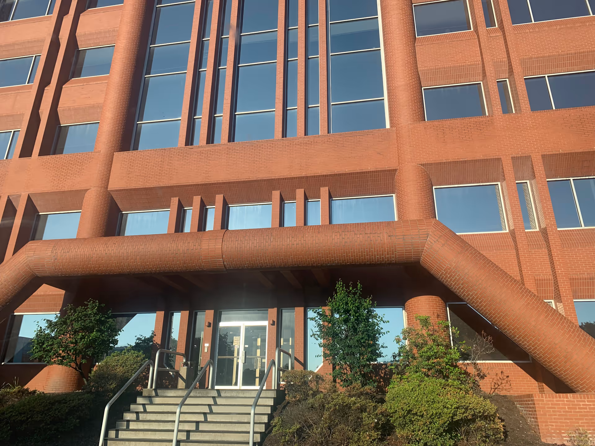 Red brick facility exterior with glass doors and landscaped entrance stairs.