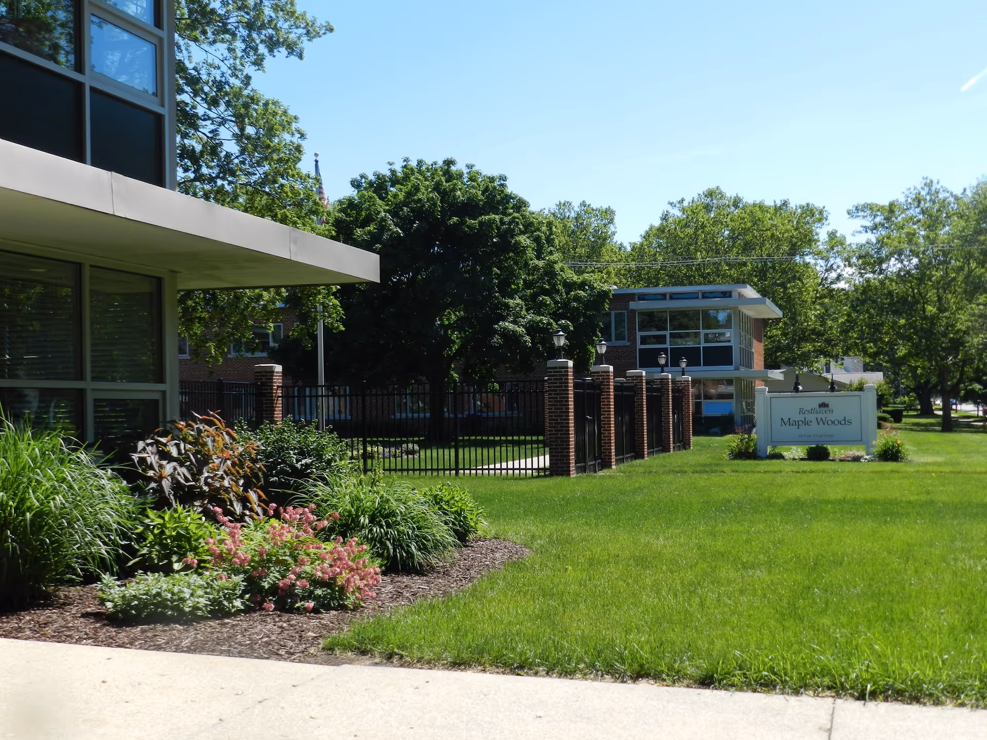 Exterior view of Resthaven Maple Woods with brick entrance pillars, sign, and manicured lawn.