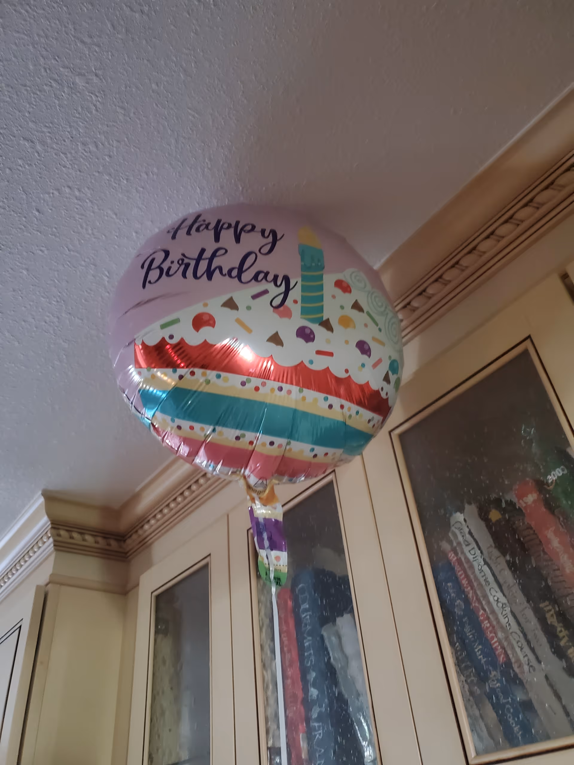 Birthday balloon near a glass-door cabinet in a decorated hallway.
