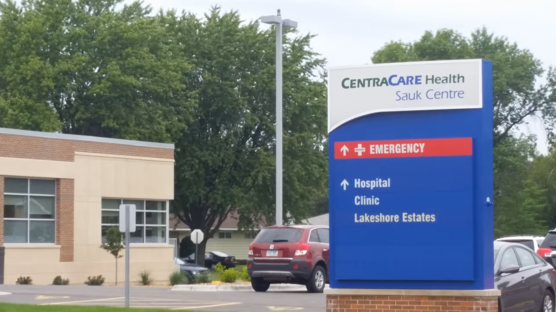 Blue CentraCare Health sign with emergency directions beside a beige building exterior.