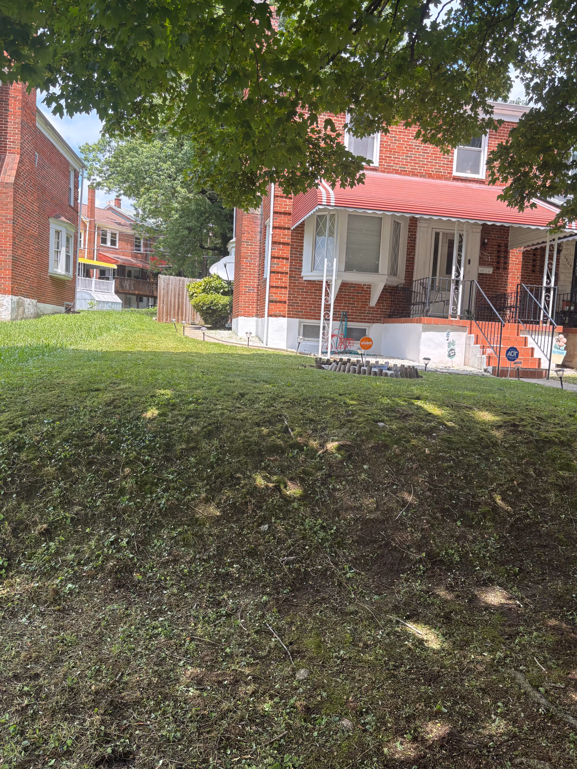Brick senior-living house with red awning, steps, and green lawn.