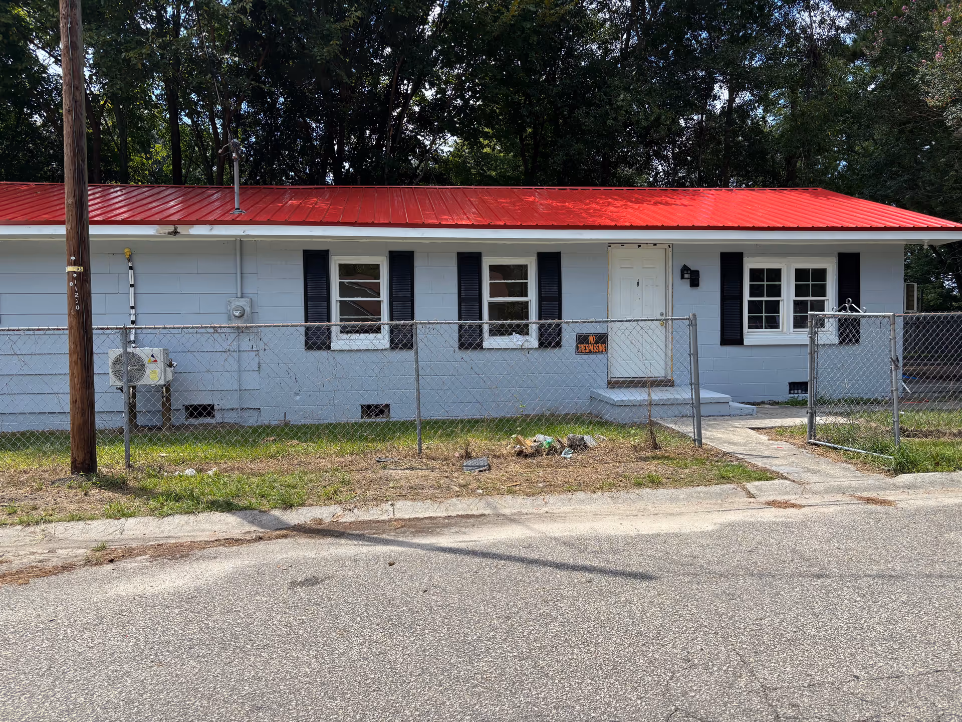 Front view of a single-story building with a red roof behind a chain-link fence.