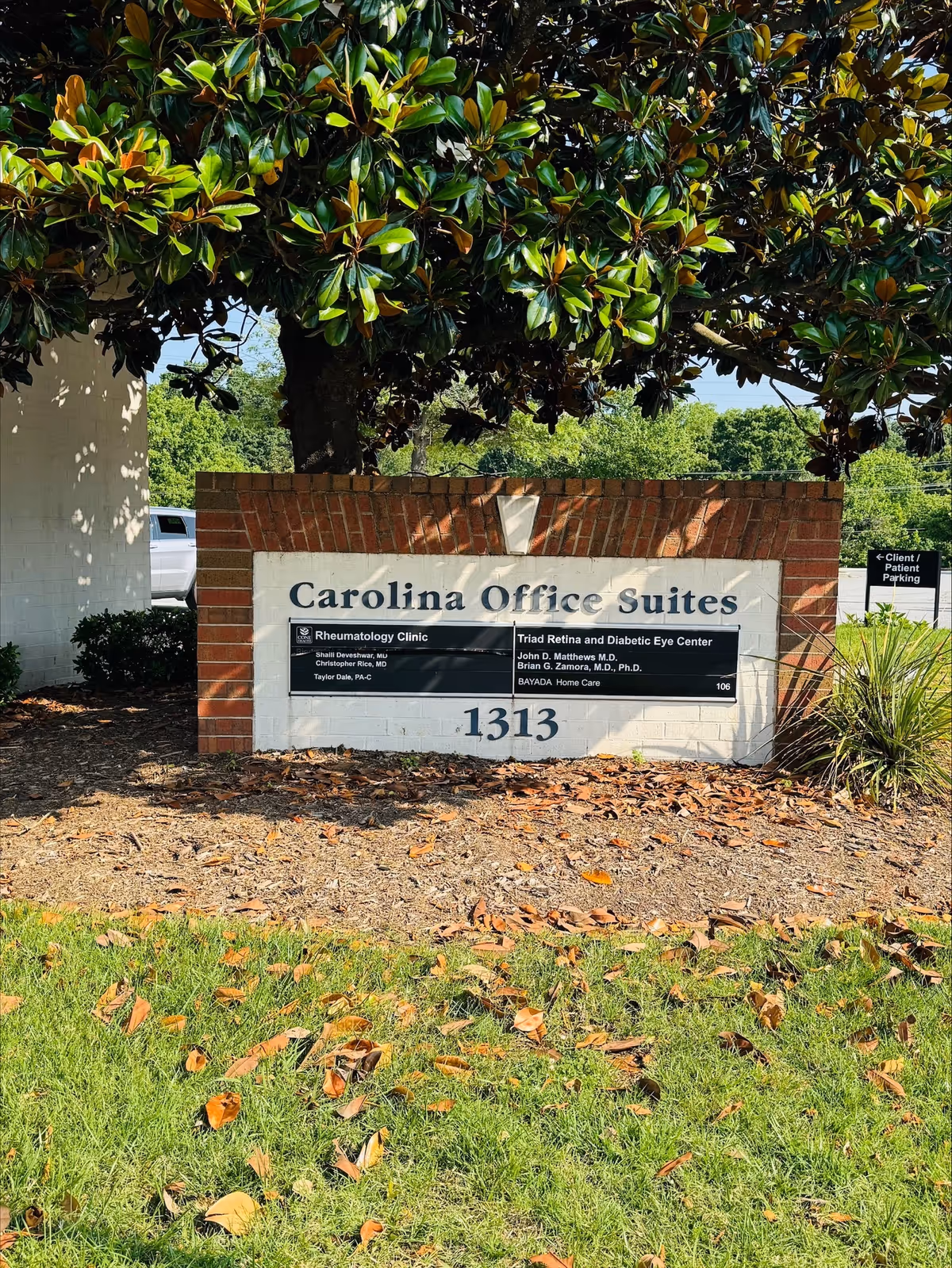 Brick sign reads Carolina Office Suites under a large tree with landscaping.