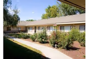 One-story beige senior living facility exterior with a paved walkway and shrubs.